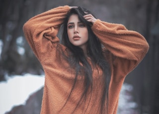 woman in orange hoodie standing near brown rock