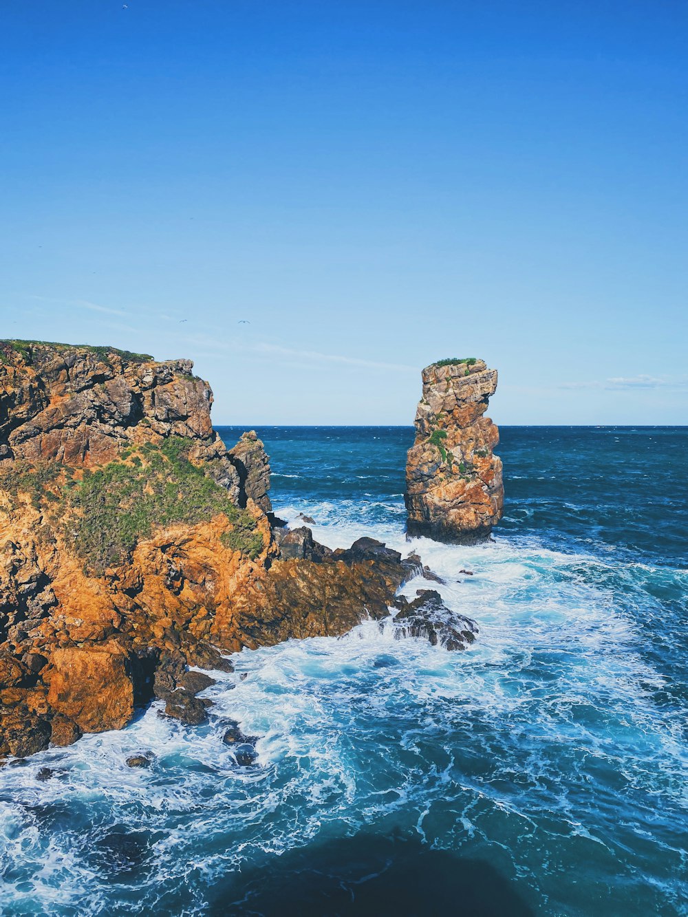 brown and green rock formation on sea under blue sky during daytime