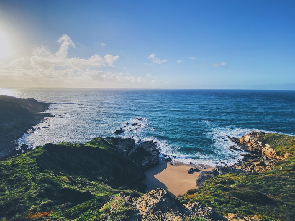 green and brown rock formation beside sea under blue sky during daytime