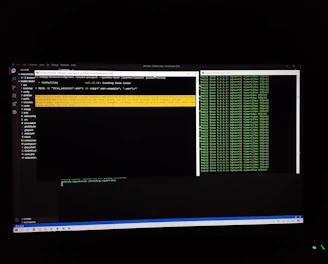 The image features a computer screen displaying a coding environment. The screen shows a text editor with various files and folders listed on the left-hand side, while the main coding area is open with a command line interface. There are green text outputs typical of command line operations performed on a black background.