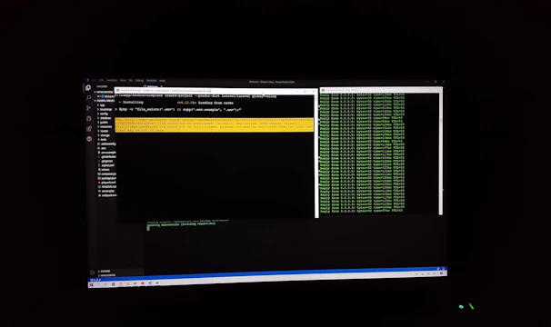 The image features a computer screen displaying a coding environment. The screen shows a text editor with various files and folders listed on the left-hand side, while the main coding area is open with a command line interface. There are green text outputs typical of command line operations performed on a black background.