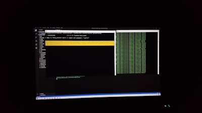 The image features a computer screen displaying a coding environment. The screen shows a text editor with various files and folders listed on the left-hand side, while the main coding area is open with a command line interface. There are green text outputs typical of command line operations performed on a black background.
