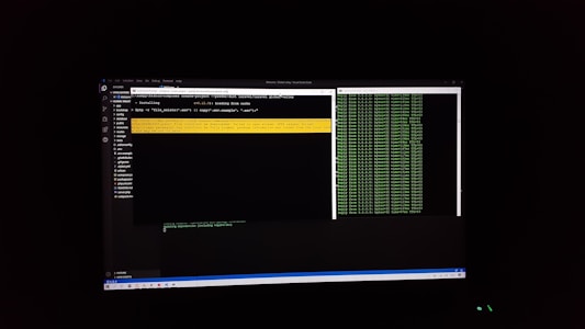 The image features a computer screen displaying a coding environment. The screen shows a text editor with various files and folders listed on the left-hand side, while the main coding area is open with a command line interface. There are green text outputs typical of command line operations performed on a black background.