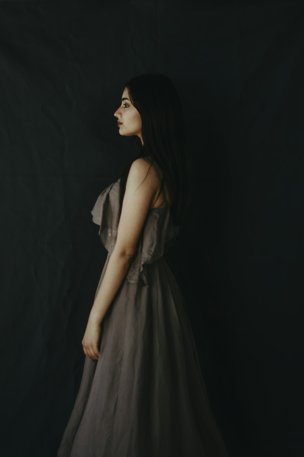 a woman in a gray dress standing in front of a black background