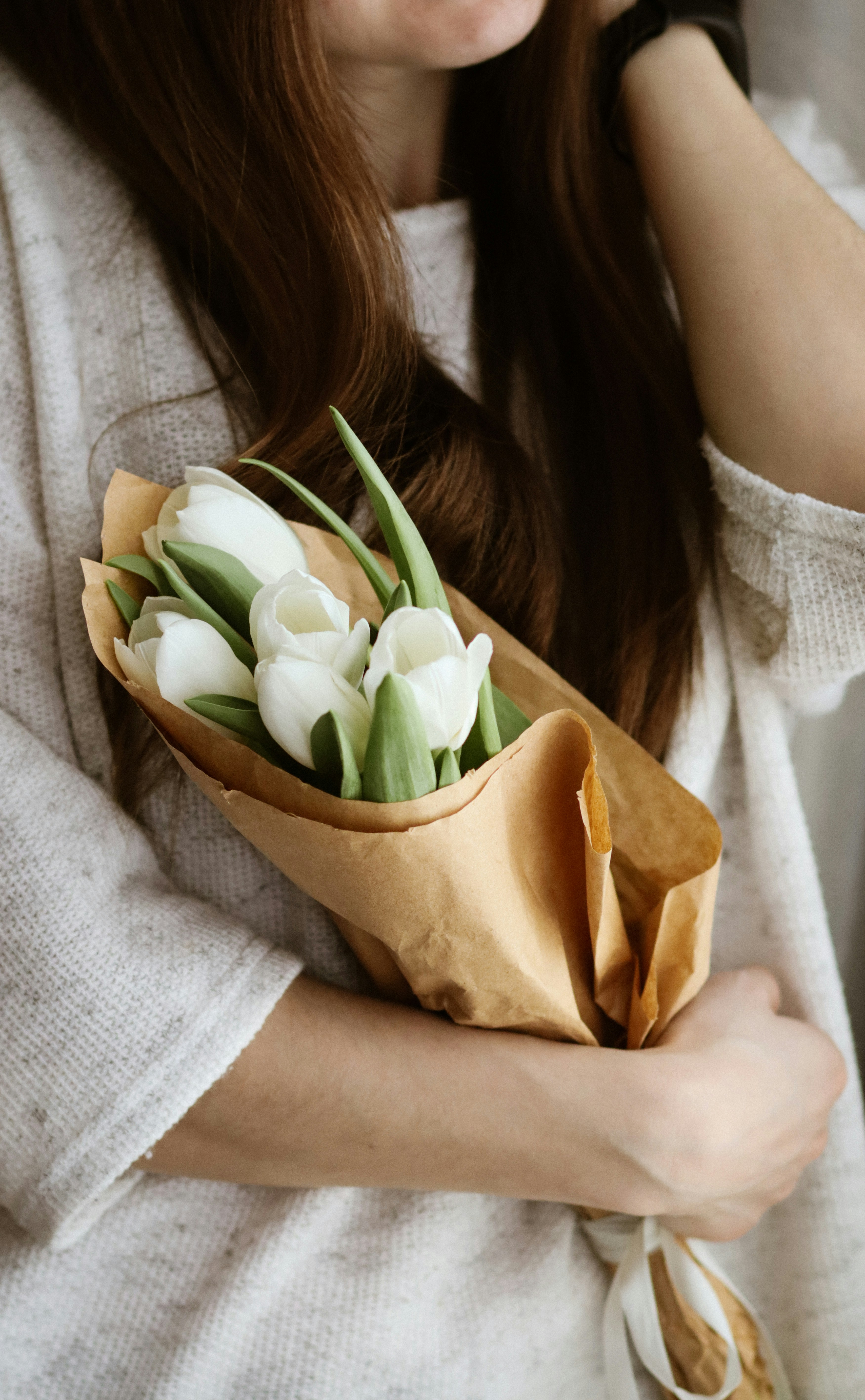 woman in white knit sweater holding white tulips bouquet