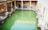 A historic bathhouse featuring a large rectangular pool filled with green water, surrounded by stone columns and walls. The architecture reflects ancient design with arches and well-preserved stone structures. Natural light casts reflections on the water, creating a serene atmosphere.
