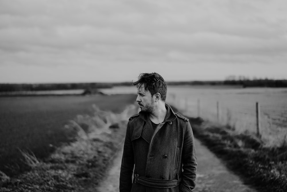 Foto en escala de grises de hombre con chaqueta de pie en el campo de hierba