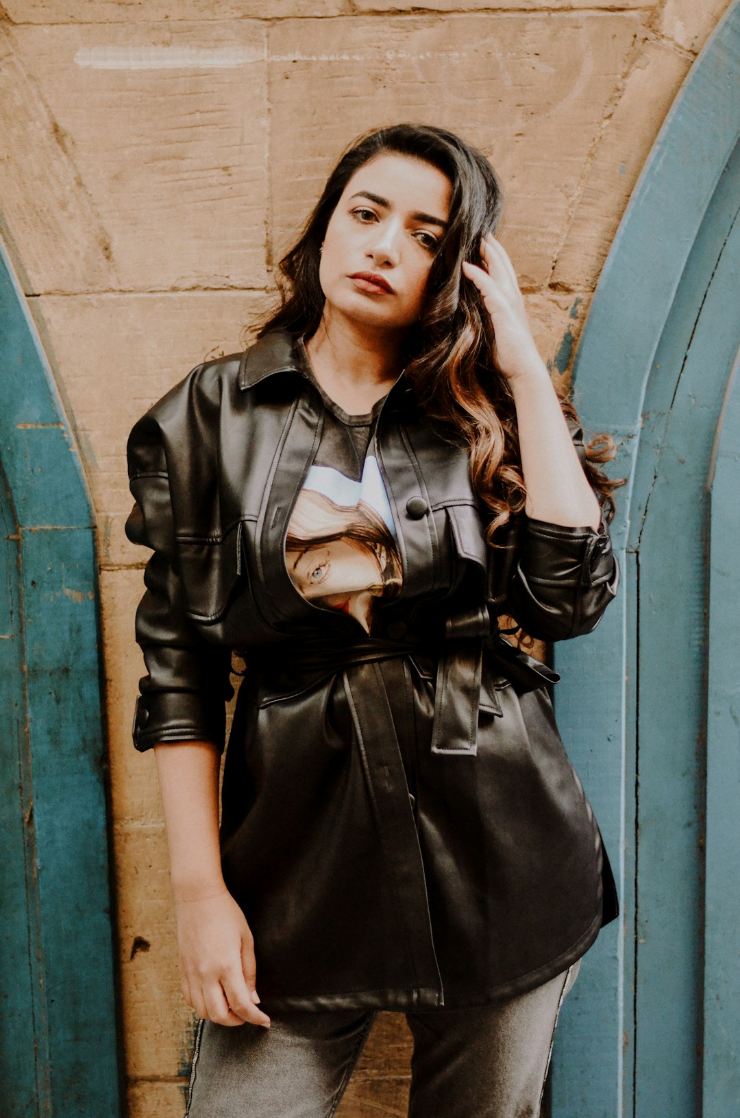 woman in black leather jacket standing beside blue wall