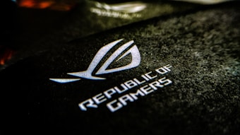 A close-up view of a textured black surface featuring the logo and text of 'Republic of Gamers.' The logo appears prominently in white, displaying a stylized, angular symbol.