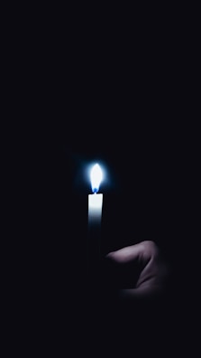 Hands gently holding a glowing candle in a dimly lit room.