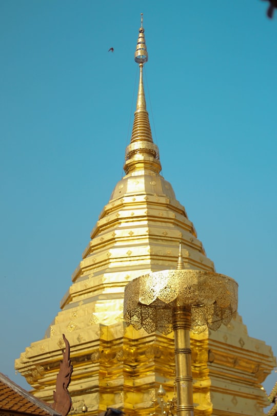 gold and white concrete building under blue sky during daytime in Wat Phrathat Doi Suthep Thailand