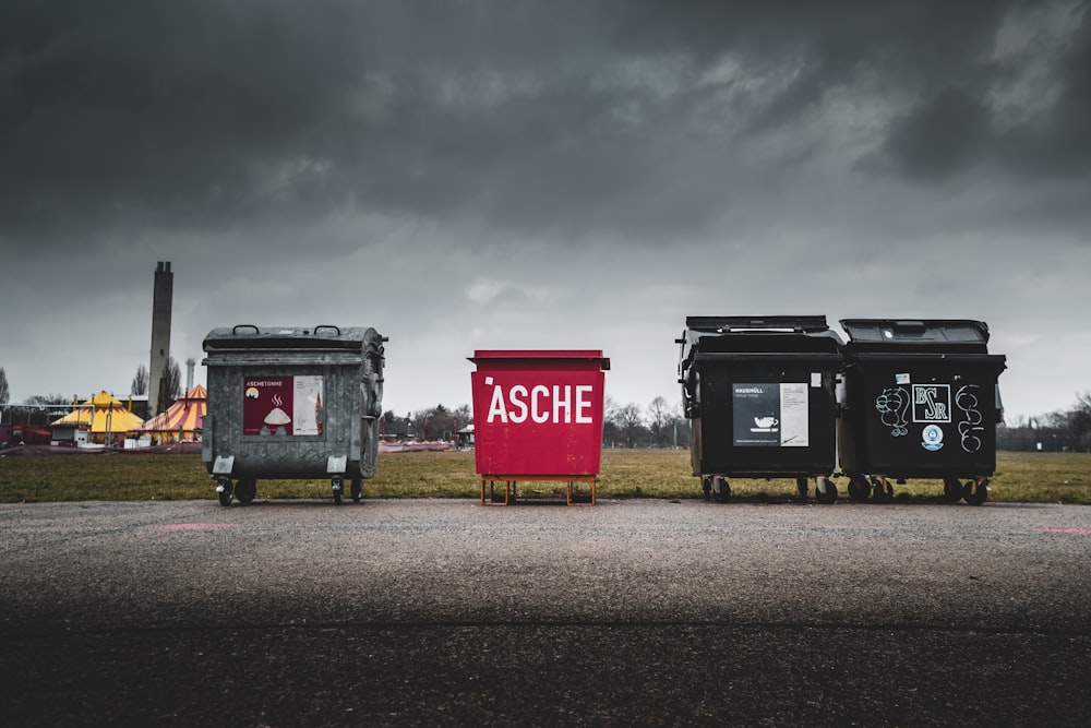 red and black trash bins on green grass field under gray cloudy sky