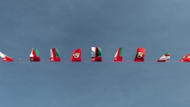 Multiple red and green flags with a white emblem are strung along a line against a clear blue sky. Some flags appear partially folded or wrapped around the line.