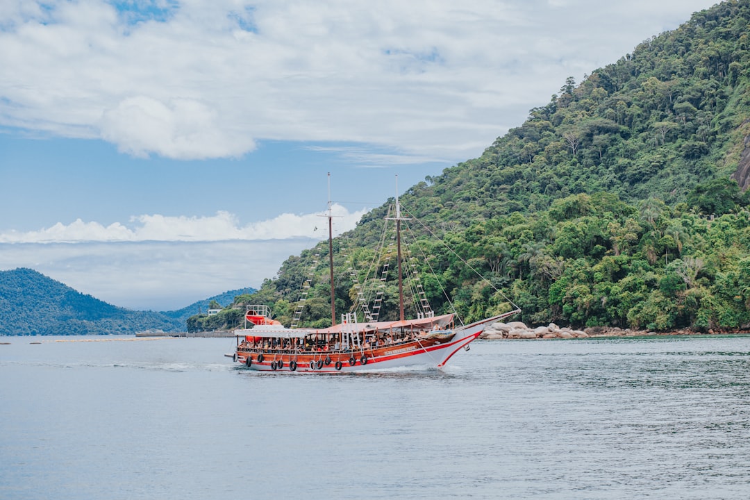 red boat on sea near green trees under white clouds and blue sky during daytime