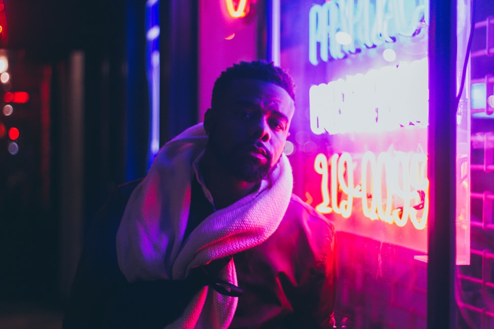 man in red hoodie standing near red and blue neon light signage