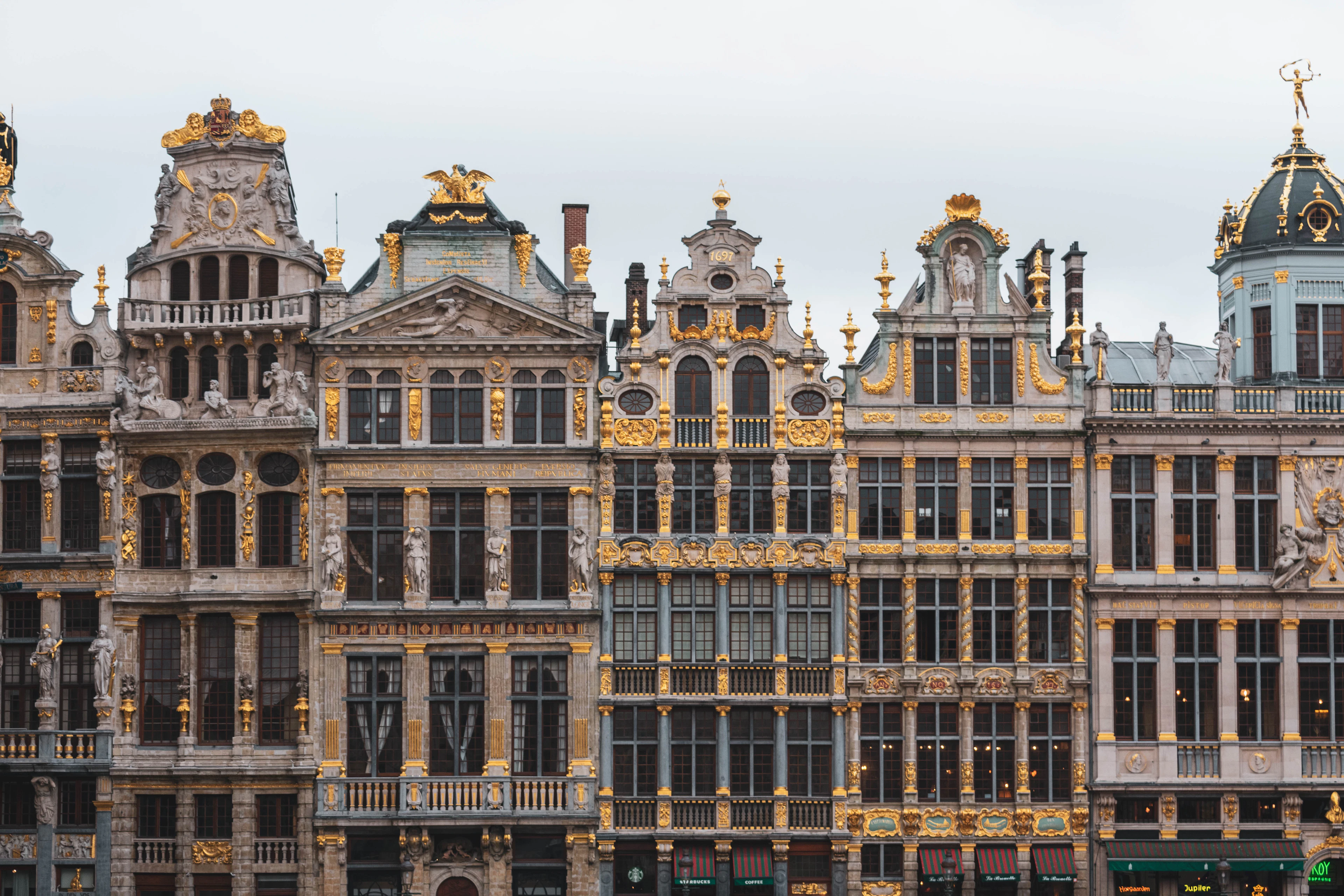 Ornate gold-gilded gable facades of Grand Place's guild houses against a pale sky.
