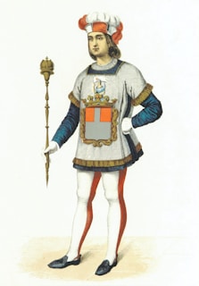A historical figure is depicted wearing a flamboyant outfit featuring a tunic with a large heraldic emblem on the front. The attire includes white and red tights, a matching hat with a feather, and a blue long-sleeve shirt underneath. The figure holds a golden scepter, standing confidently with one hand on the hip.