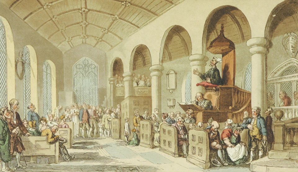 Large crowd seated in rows facing elevated stage with speaker delivering speech indoors