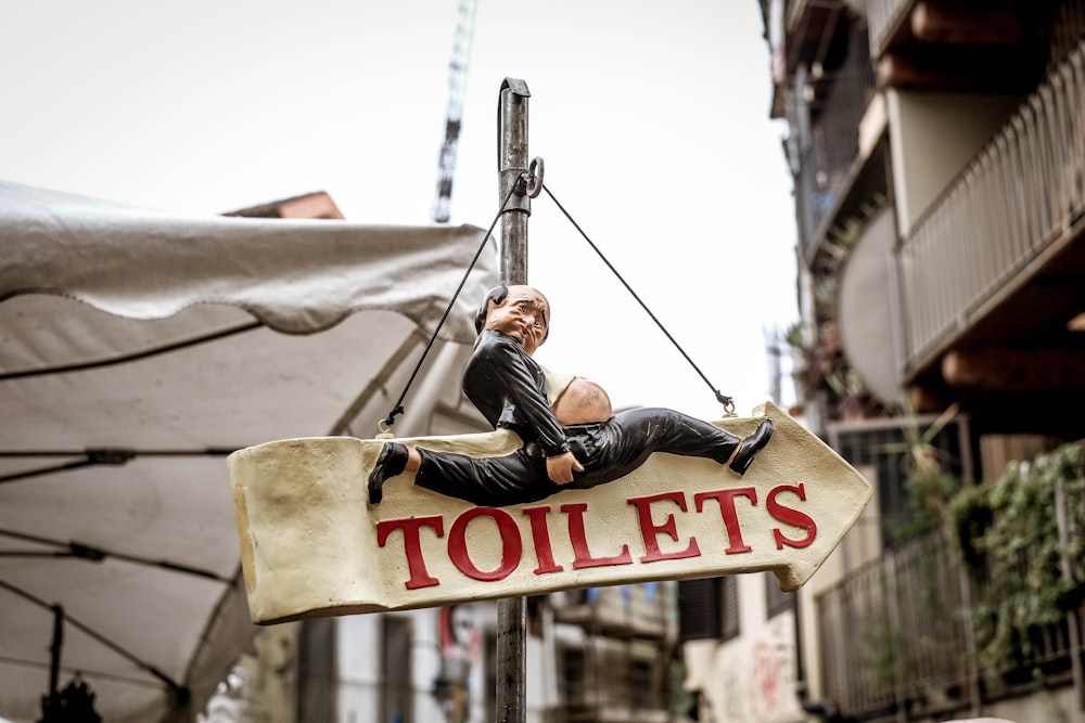 man in black leather jacket and black pants sitting on brown wooden hanging signage during daytime