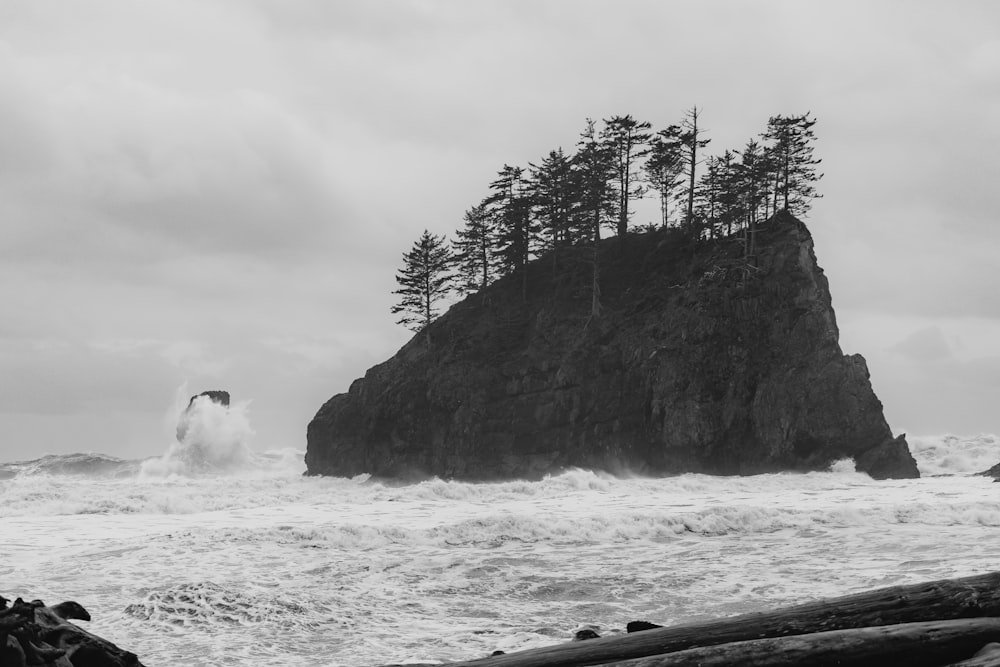grayscale photo of man and woman standing on rock formation near body of water