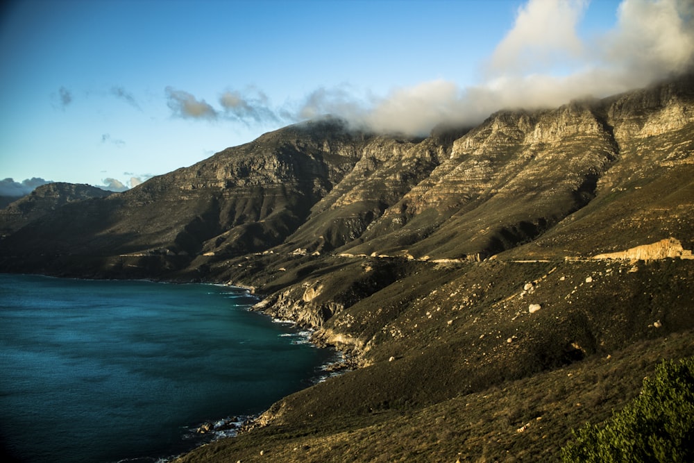 green and brown mountains beside blue sea under blue sky during daytime