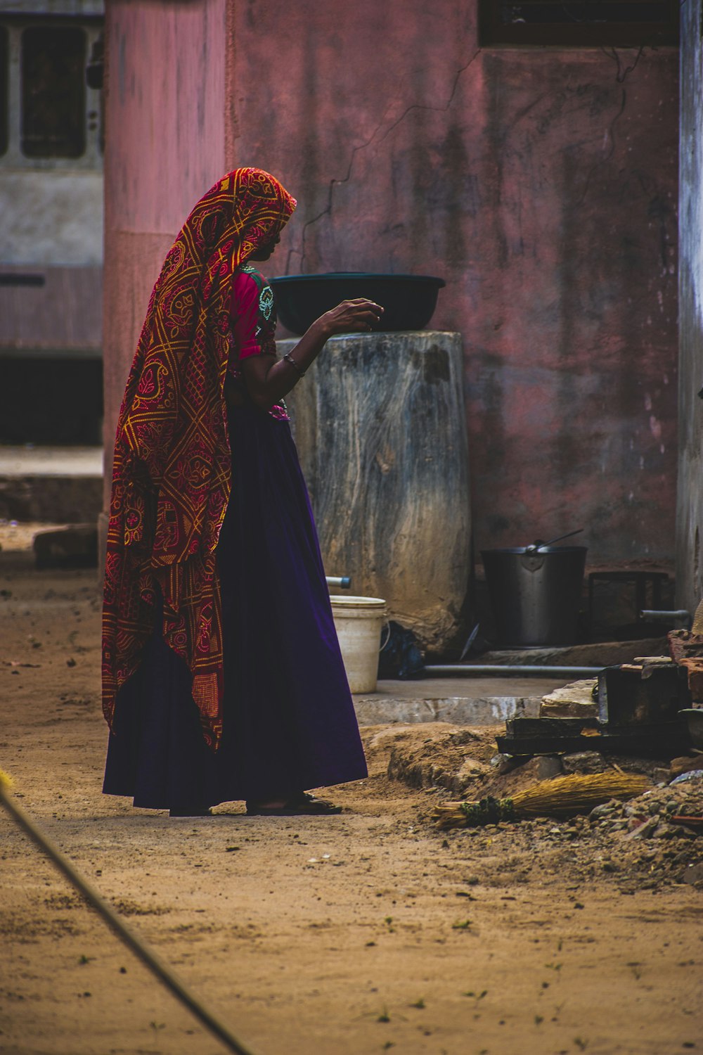 Femme en robe rouge et bleue debout près d’un poteau en bois brun