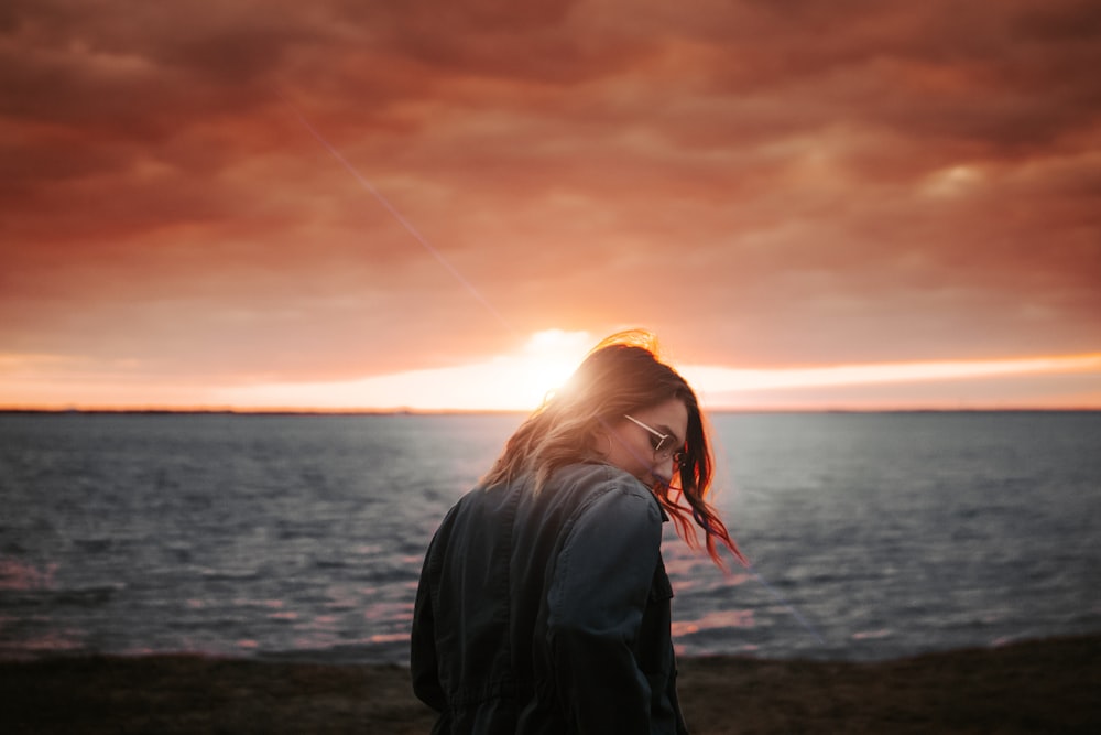 Frau in schwarzer Jacke beim Sonnenuntergang am Strand