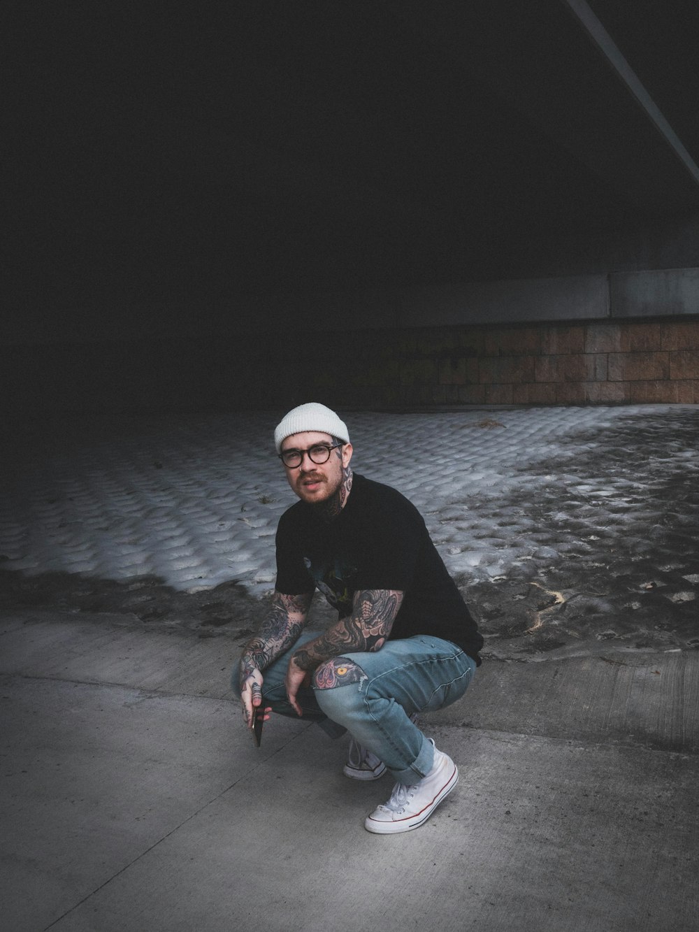 man in black jacket and blue denim jeans sitting on gray concrete floor