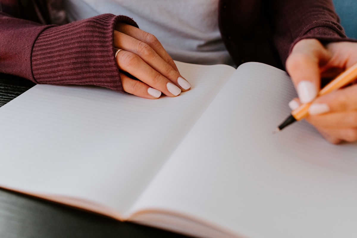 Person writing in a notebook at a desk while planning a daily supplement routine