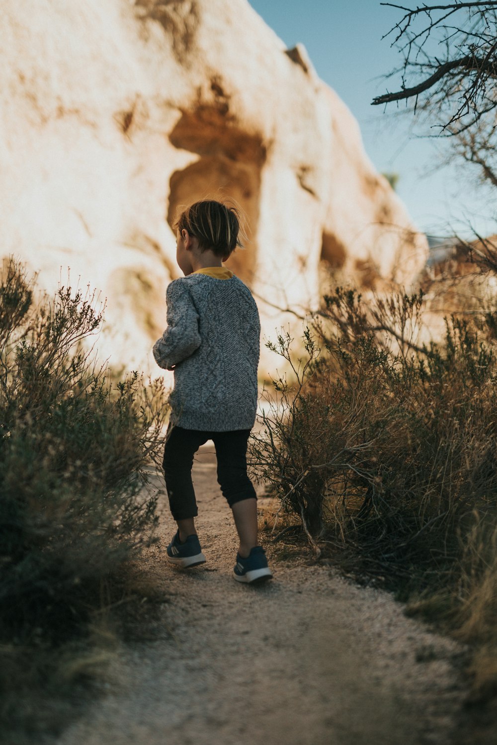 woman in gray sweater standing near brown rock formation during daytime