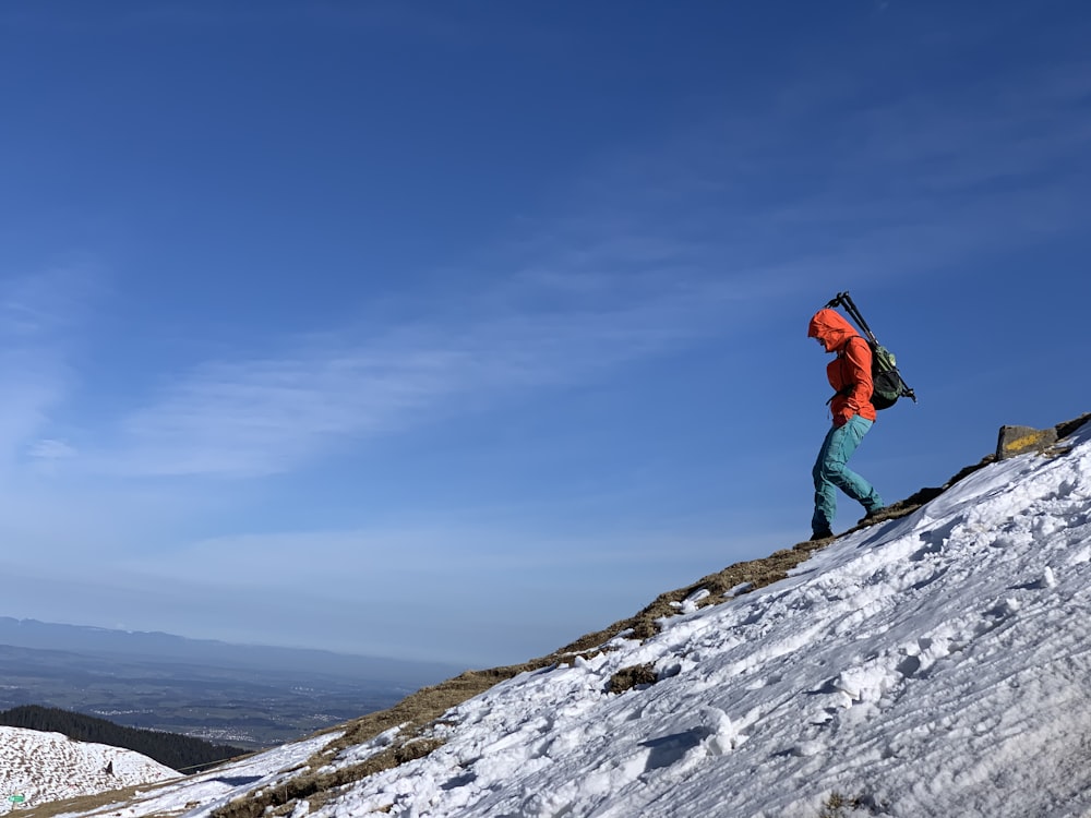 person in red jacket and black pants standing on snow covered mountain during daytime