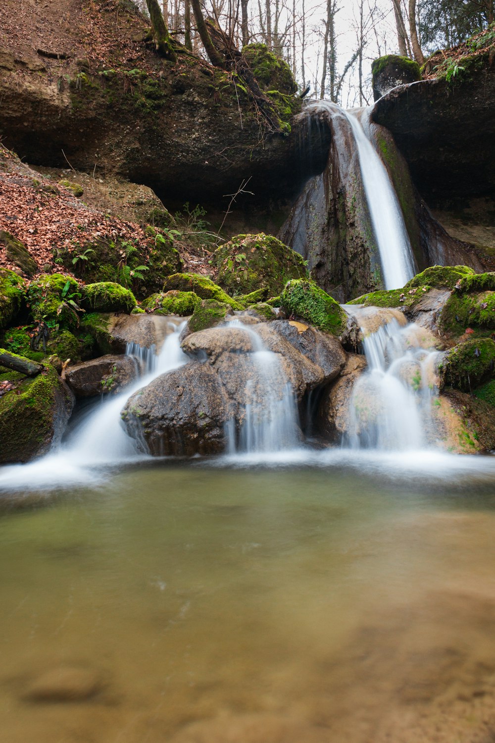 Wasser fällt inmitten von grünen, moosbedeckten Felsen