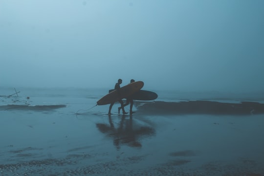 man in black shirt holding brown surfboard walking on beach during daytime in Pichilemu Chile