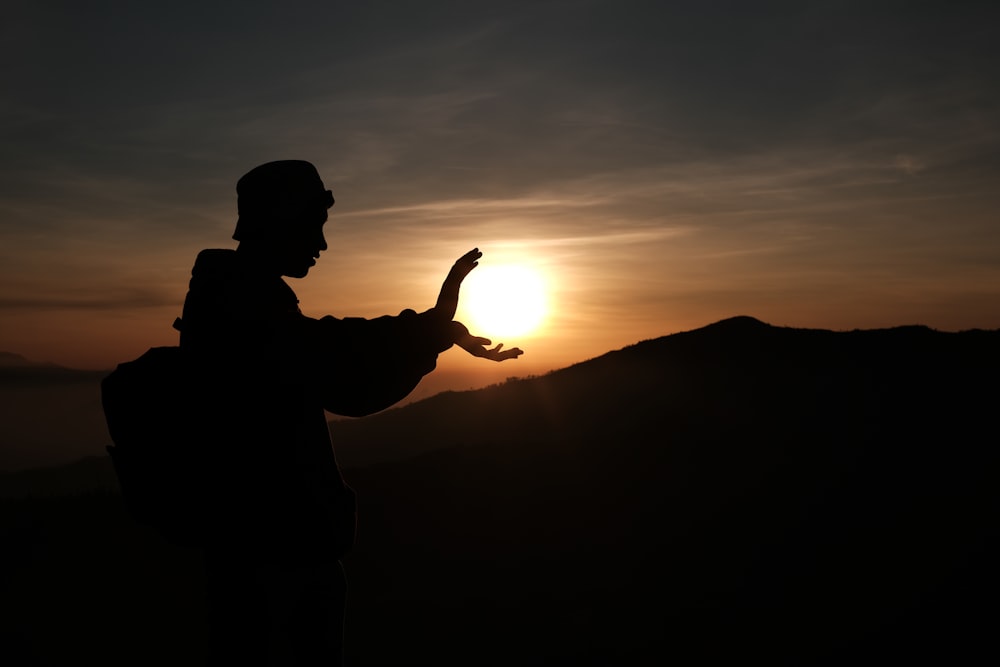 夕暮れ時の山の頂上に立つ男のシルエット