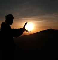 silhouette of man standing on top of mountain during sunset