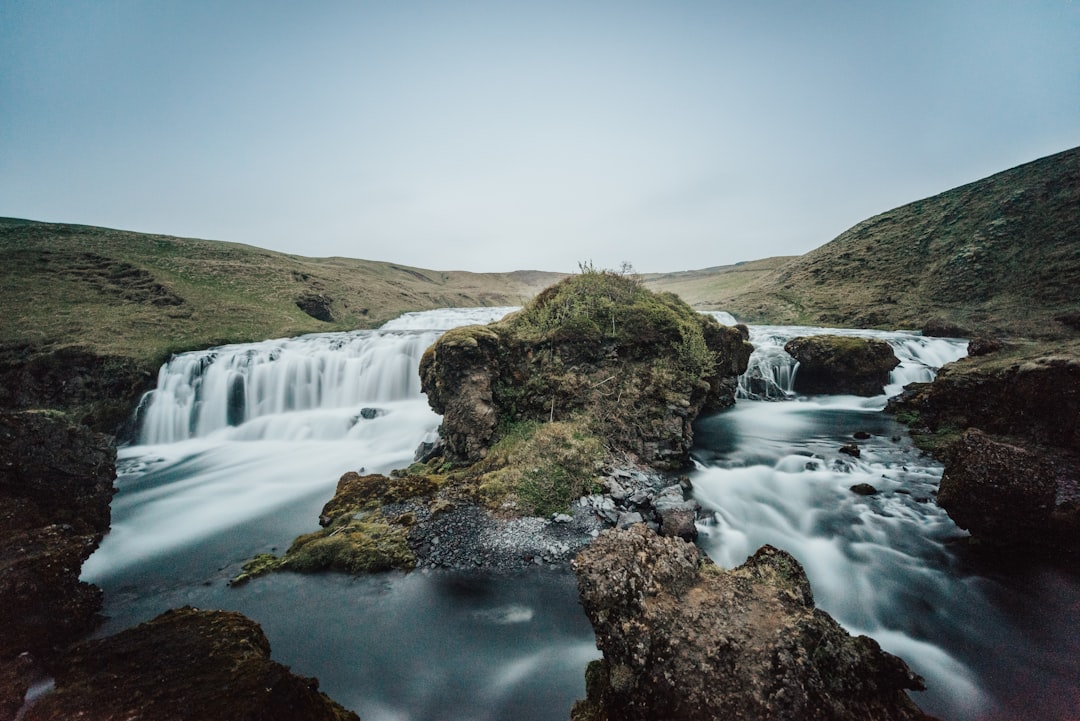 green grass field near waterfalls under white sky during daytime