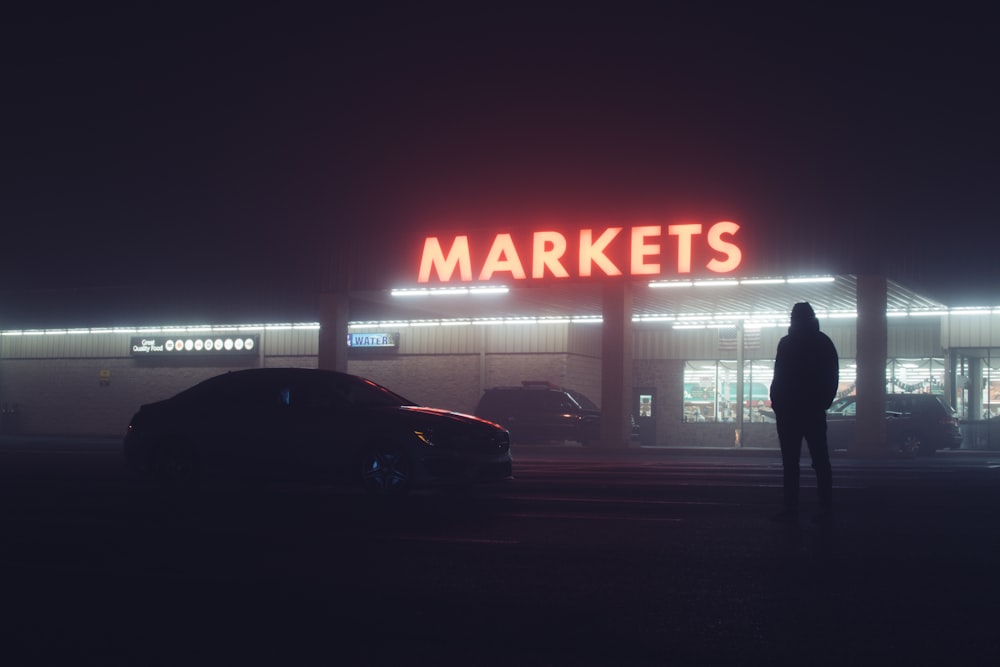 man in black jacket standing near red and white UNK neon signage