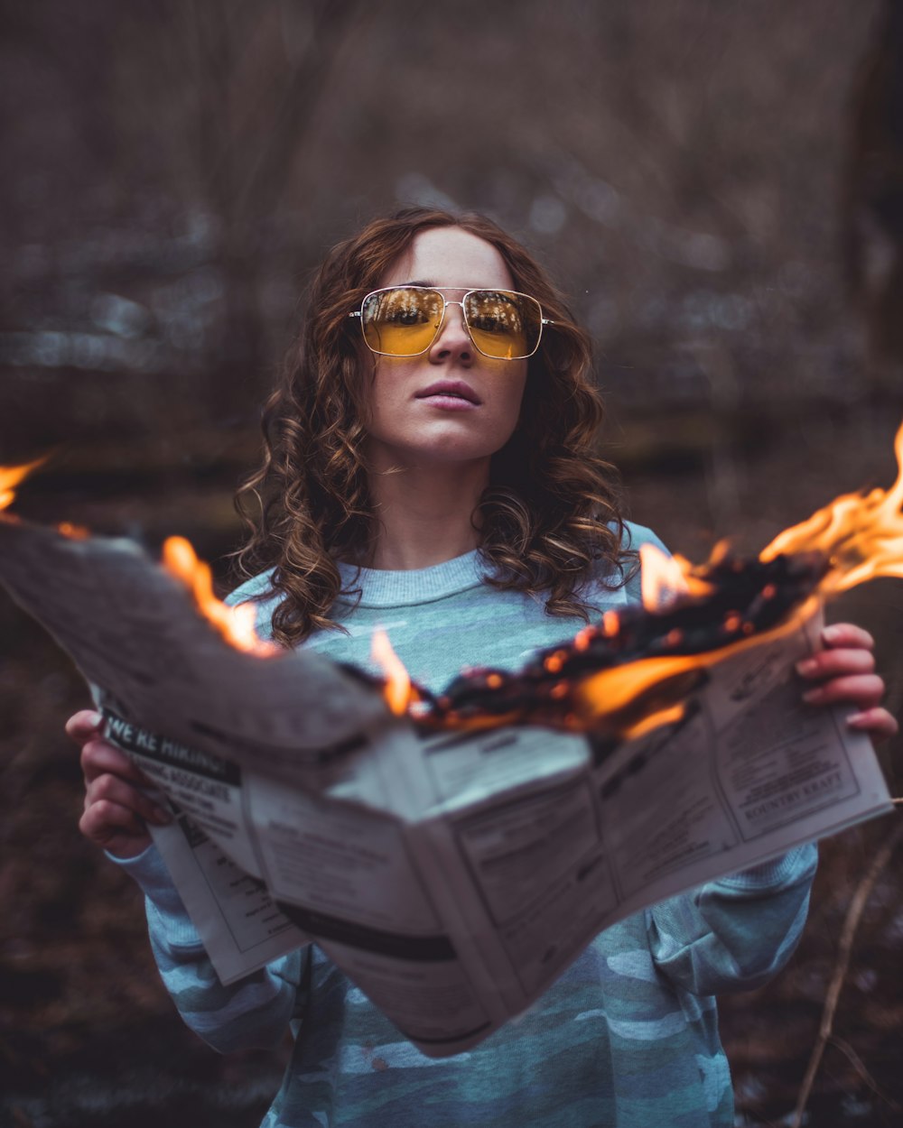 woman in blue denim jacket wearing brown sunglasses holding burning paper