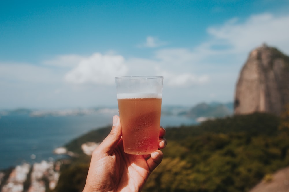 person holding clear drinking glass with brown liquid