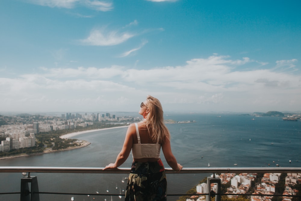 woman in white tank top and black skirt standing on balcony during daytime