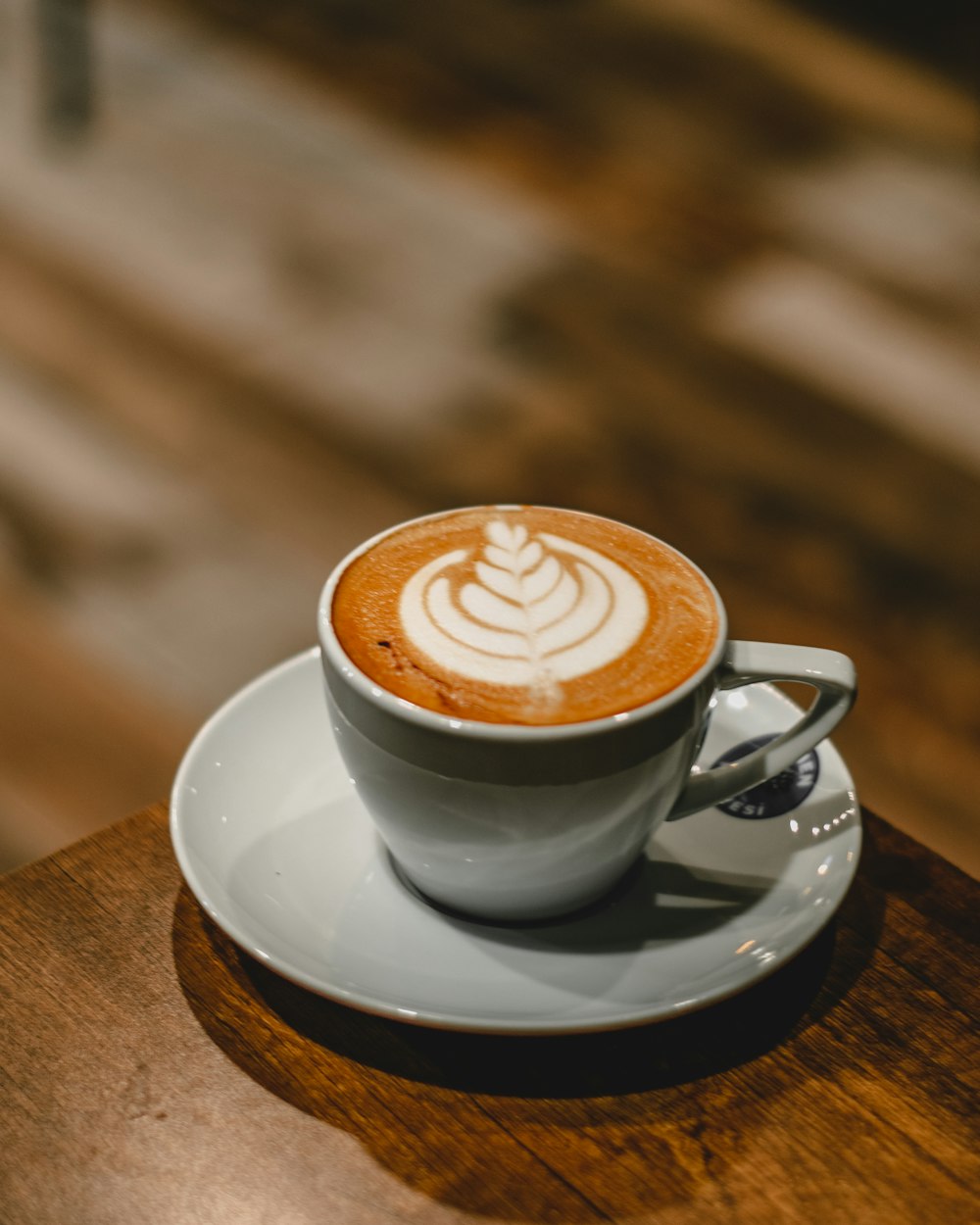 weiße Keramiktasse mit Untertasse auf braunem Holztisch