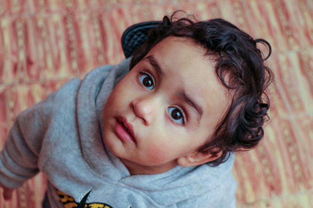 boy in gray hoodie lying on brown and white textile