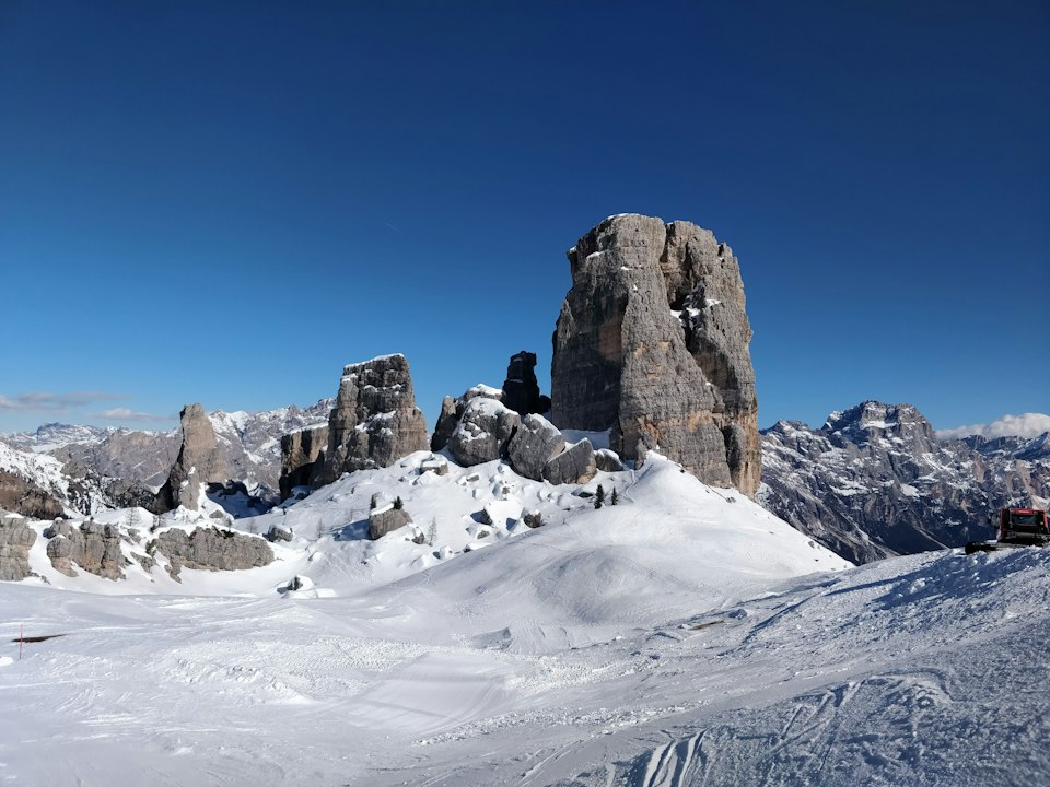 The Cinque Torri rock towers rising from a snow-dusted alpine meadow in the Dolomites