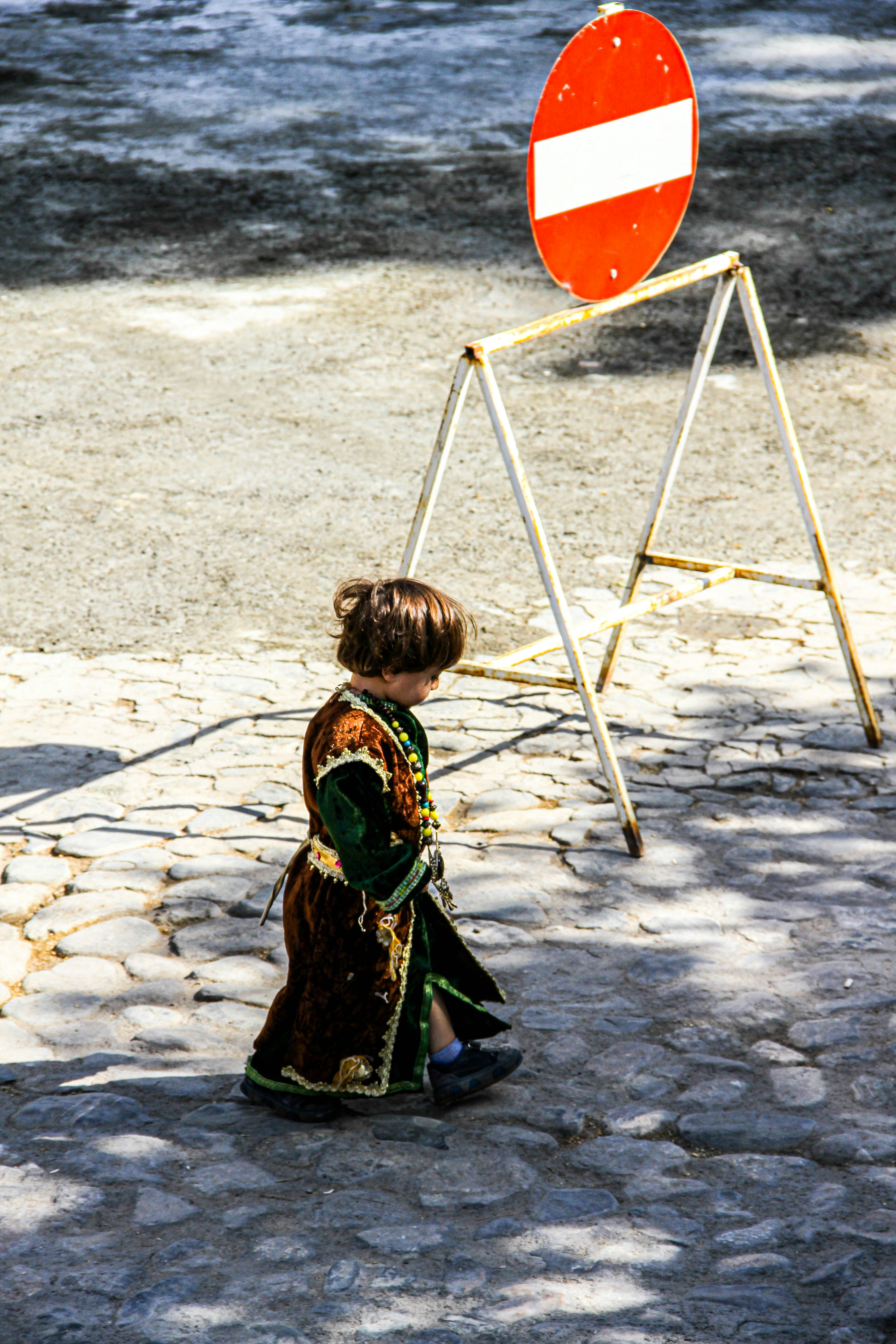 girl in black and brown dress holding orange umbrella walking on gray sand during daytime