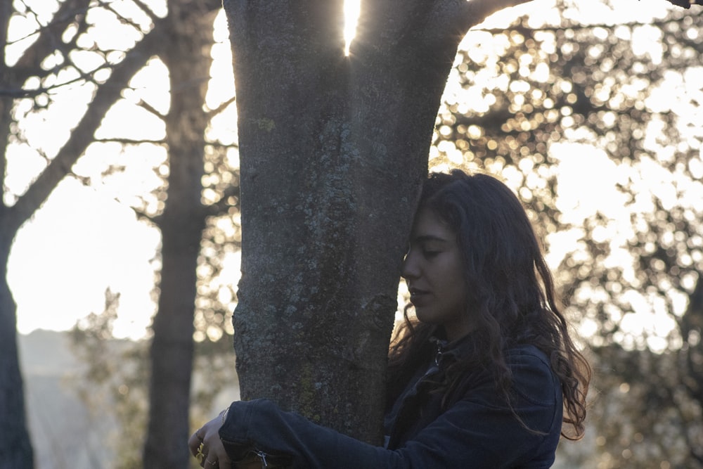 woman in blue jacket leaning on tree