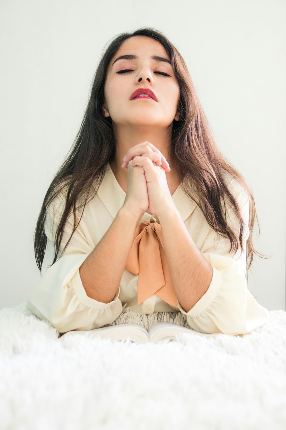 woman in white long sleeve shirt lying on white textile