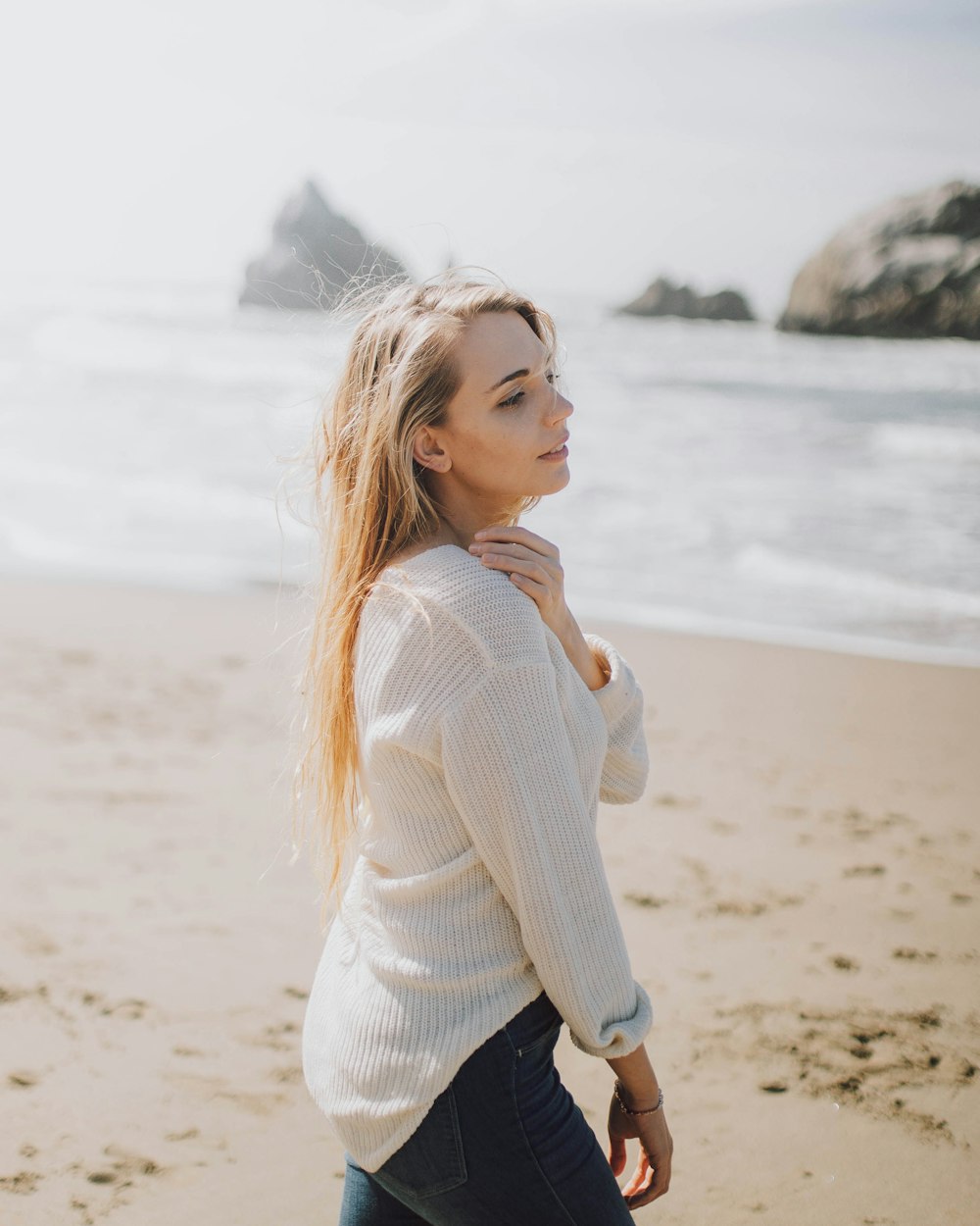 donna in maglione bianco in piedi sulla spiaggia durante il giorno