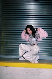 woman in pink hoodie and white pants sitting on floor