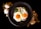 Two sunny-side-up eggs are placed on a bed of greens on a dark round plate. To the left of the plate, two whole eggs and some golden granules are scattered on a black surface. To the right, there is a decorative arrangement of dried flowers and wooden sticks.