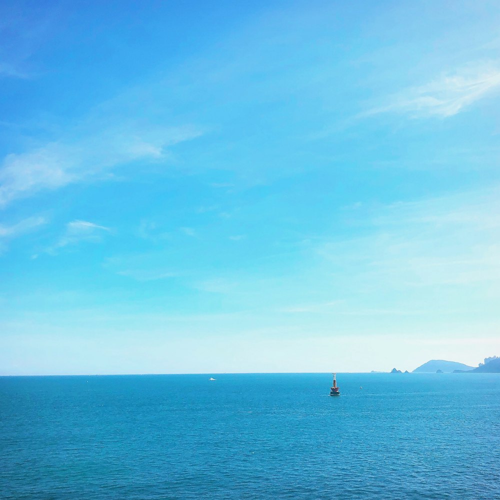 Person im schwarzen Hemd, die tagsüber auf blauem Meer unter blauem Himmel steht